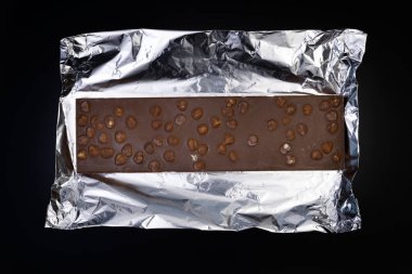 Tatlı ve lezzetli çikolata, gümüş folyoda fındıklar ve siyah arka planda fotoğraf.