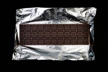 Gümüş folyo üzerine tatlı ve lezzetli çikolata. Yukarıdan çekilmiş siyah arka plan fotoğrafı.