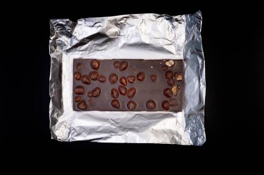 Tatlı ve lezzetli çikolata, gümüş folyoda fındıklar ve siyah arka planda fotoğraf.