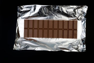 Gümüş folyo üzerine tatlı ve lezzetli çikolata. Yukarıdan çekilmiş siyah arka plan fotoğrafı.