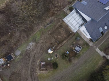 Küçük, sarı kazıcının hava aracı görüntüsü büyük bir bahçede duruyor ve Avusturya 'da bir havuz için çukur kazıyor.