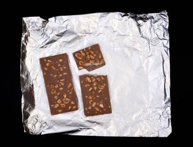 Tatlı ve lezzetli çikolata, gümüş folyoda fındıklar ve siyah arka planda fotoğraf.