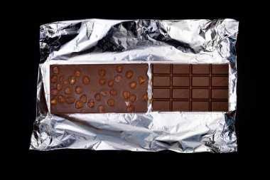 Tatlı ve lezzetli çikolata, gümüş folyoda fındıklar ve siyah arka planda fotoğraf.