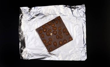 Tatlı ve lezzetli çikolata, gümüş folyoda fındıklar ve siyah arka planda fotoğraf.