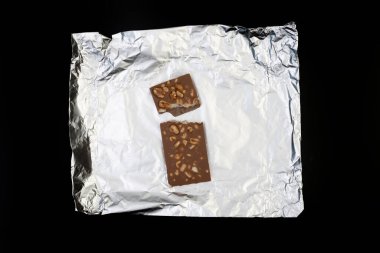 Tatlı ve lezzetli çikolata, gümüş folyoda fındıklar ve siyah arka planda fotoğraf.