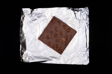 Tatlı ve lezzetli çikolata, gümüş folyoda fındıklar ve siyah arka planda fotoğraf.