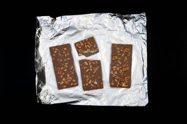 Tatlı ve lezzetli çikolata, gümüş folyoda fındıklar ve siyah arka planda fotoğraf.