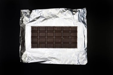 Gümüş folyo üzerine tatlı ve lezzetli çikolata. Yukarıdan çekilmiş siyah arka plan fotoğrafı.