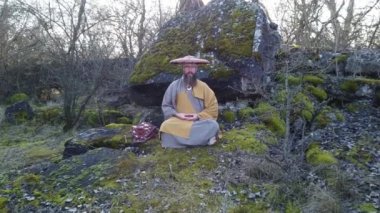 Sakallı Avrupalı bir adam doğada geleneksel Japon, Shugendo kıyafetleriyle meditasyon yapıyor.