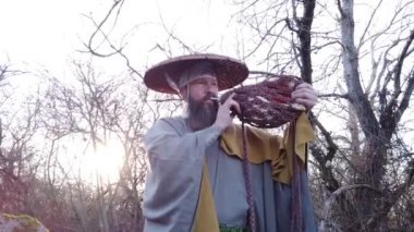 Sakallı Avrupalı bir adam doğada geleneksel Japon, Shugendo kıyafetleriyle meditasyon yapıyor.