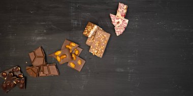 Birçok farklı çikolata çeşidi siyah bir ahşap tabakta yatar, yukarıdan çekilmiş bir fotoğraf.