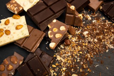 Bir sürü çikolata çeşidi ve fındık ve kakao tozu gibi çeşitli malzemeler yukarıdan çekilen siyah bir tahta tabakta duruyor.