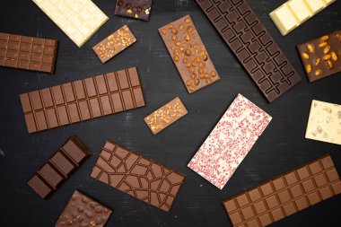 Farklı tatlı, narin çikolatalar siyah ahşap bir arka planda yaratıcı bir şekilde uzanır.