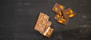 Birçok farklı çikolata çeşidi siyah bir ahşap tabakta yatar, yukarıdan çekilmiş bir fotoğraf.