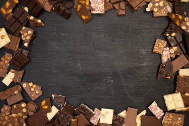 Birçok farklı çikolata çeşidi siyah bir ahşap tabakta yatar, yukarıdan çekilmiş bir fotoğraf.