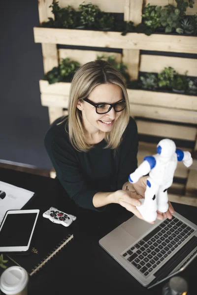 pretty young blond woman sits in a sustainable office and works with a small robot
