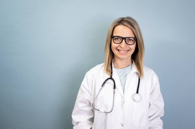 Güzel sarışın çekici bayan doktor mavi arka planda poz veriyor.