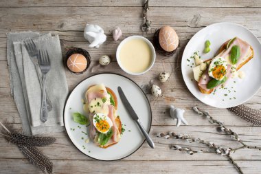 Paskalya kahvaltısı, tereyağlı ve peynirli Paskalya ekmeği, yumurta ve soğanlı jambon ve hafif ahşap arka planda Paskalya süslemesi olan fesleğen.