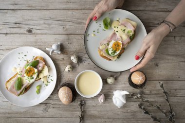 Paskalya kahvaltısı, tereyağlı ve peynirli Paskalya ekmeği, yumurta ve soğanlı jambon ve hafif ahşap arka planda Paskalya süslemesi olan fesleğen.