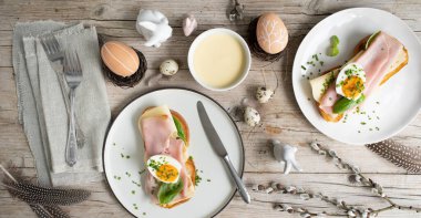 Paskalya kahvaltısı, tereyağlı ve peynirli Paskalya ekmeği, yumurta ve soğanlı jambon ve hafif ahşap arka planda Paskalya süslemesi olan fesleğen.