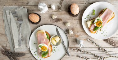 Paskalya kahvaltısı, tereyağlı ve peynirli Paskalya ekmeği, yumurta ve soğanlı jambon ve hafif ahşap arka planda Paskalya süslemesi olan fesleğen.