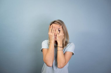 Güzel sarışın, çekici bir kadın mavi arka planda poz veriyor ve korkuyor.