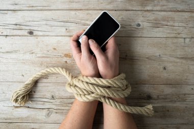 Bir adamın elleri iple bağlanır ve elinde bir akıllı telefon, konsept bağımlılığı, sosyal medya, yukarıdan çekilmiş bir fotoğraf tutar.
