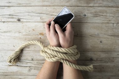 Bir adamın elleri iple bağlanır ve elinde bir akıllı telefon, konsept bağımlılığı, sosyal medya, yukarıdan çekilmiş bir fotoğraf tutar.