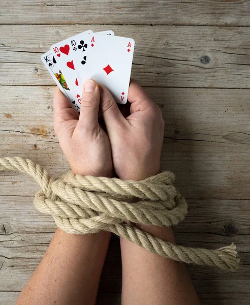 Hands of man are tied with a rope and in his hands he holds playing cards, concept addiction, Gambling addiction, photo taken from above