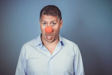 Orta yaşlı, mavi gömlekli ve kırmızı burunlu bir adam stüdyoda mavi arka planda poz veriyor.