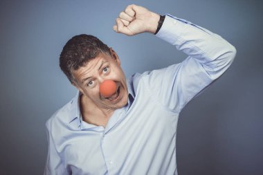 Orta yaşlı, mavi gömlekli ve kırmızı burunlu bir adam stüdyoda mavi arka planda poz veriyor.