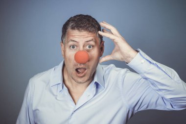 Orta yaşlı, mavi gömlekli ve kırmızı burunlu bir adam stüdyoda mavi arka planda poz veriyor.