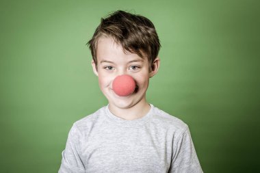 Yeşil elli, kırmızı burunlu yakışıklı okul çocuğu yeşil arka planda poz veriyor.