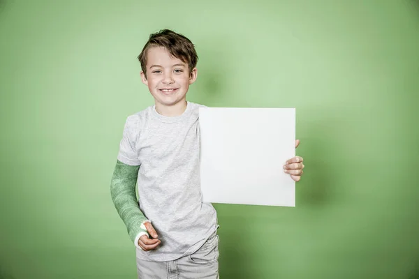 緑の背景の前に白い板を持つ緑の手の石膏ボードを持つクールな少年 — ストック写真