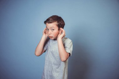 Gri tişörtlü havalı çocuk stüdyoda mavi arka planda poz veriyor. 