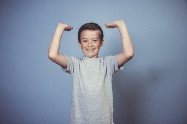 Gri tişörtlü havalı çocuk stüdyoda mavi arka planda poz veriyor. 