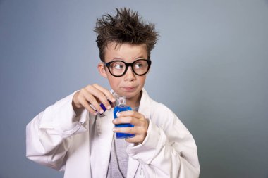 Vahşi saçlı, beyaz önlüklü havalı çocuk elinde mavi sıvıyla küçük bir şişe tutuyor ve çılgın bir bilim adamına benziyor.