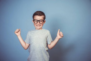 Kalın siyah gözlüklü havalı okul çocuğu stüdyoda mavi arka planda poz veriyor.