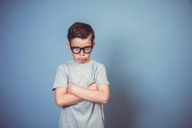 Kalın siyah gözlüklü havalı okul çocuğu stüdyoda mavi arka planda poz veriyor.