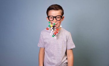 Siyah gözlüklü havalı çocuk mavi arka planda duruyor ve moleküllerin modelini tutuyor.