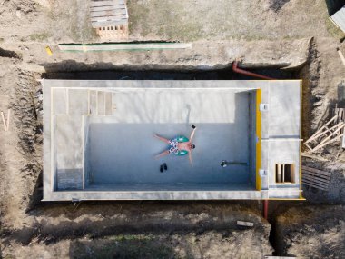 Yüzme şortlu bir adam yüzen bir lastiğin üzerinde havuzun içinde yatıyor ve insansız hava aracıyla selfie çekiyor.