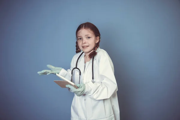 青い背景の前に緑の手袋とデジタルタブレットで医者の格好をした美しい少女 — ストック写真