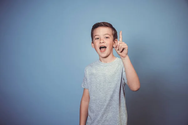 グレーのTシャツを着た若い男の子がスタジオの青の背景の前でポーズをとっています — ストック写真