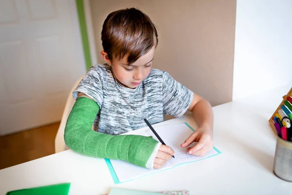 cool boy with green arm cast is sitting in his room and is writing something and is doing housework