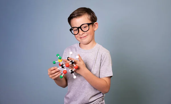 青い背景には冷たい黒眼鏡の少年が分子の模型を持って立っています — ストック写真