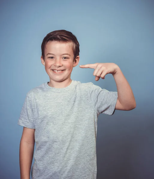 グレーのTシャツを着た若い男の子がスタジオの青の背景の前でポーズをとっています — ストック写真