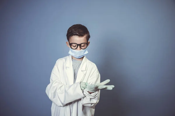 マウスガード付きのクールな男の子 スタジオで青の背景に白い研究室のコートや医師のコートと黒眼鏡とゴム手袋 — ストック写真