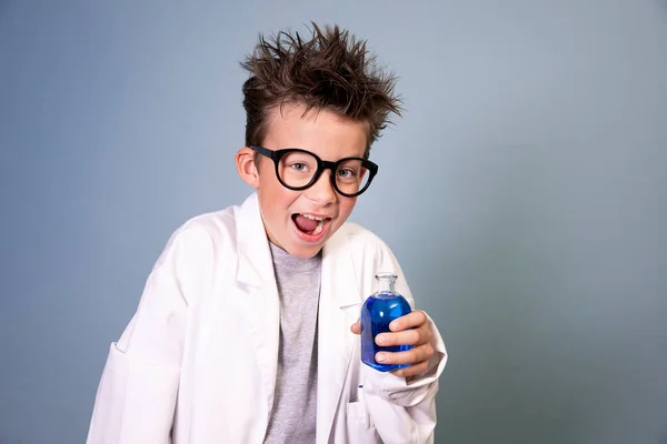 野生の髪と白いコートのクールな男の子は青い液体と小さなボトルを保持し 狂っ科学者のように見えます — ストック写真