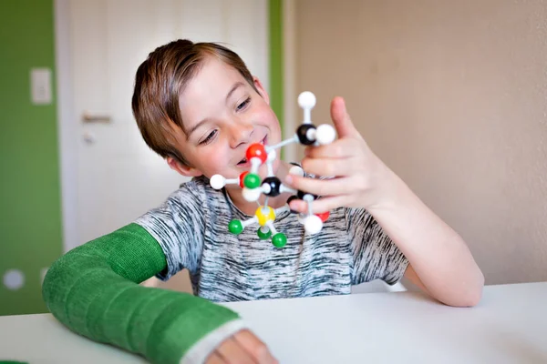 彼の部屋には緑の腕の石膏のキャストを持つクールな学童が座っており 分子のモデルと遊ぶ — ストック写真