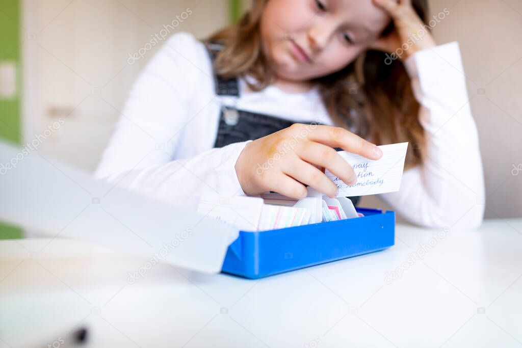 pretty young schoolgirl sitting on her desk in her room at home learning english vocabulary using flashcards during corona time